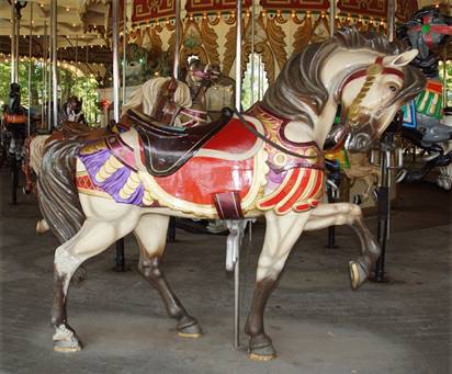 A horse drawn carriage in front of a carousel

Description automatically generated